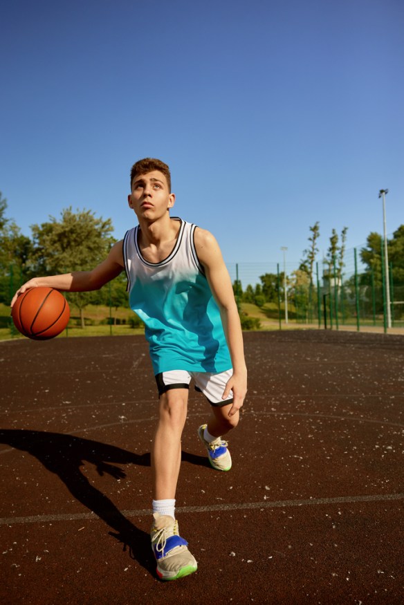 Young teenager training on street court playing basketball